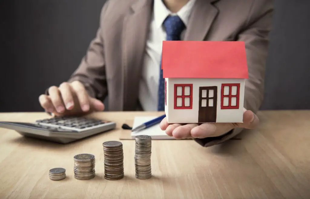 A person holding a house model while using a calculator