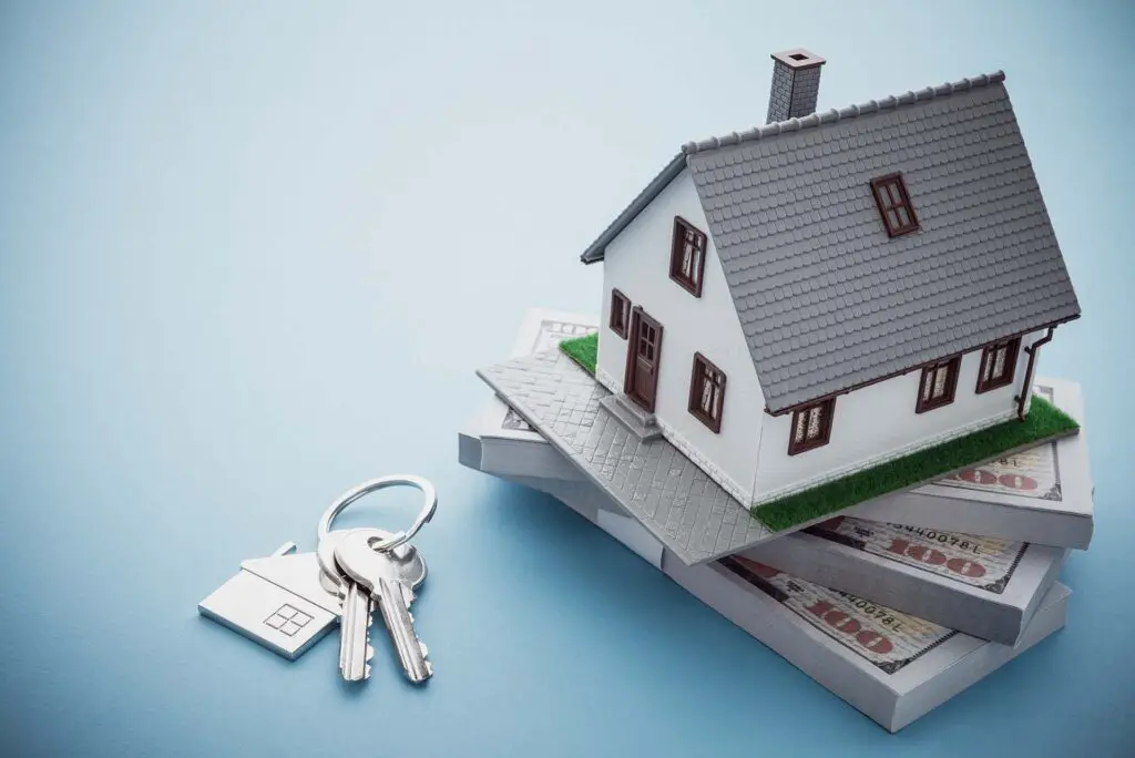 Model of a house on a pile of money and keys next to it