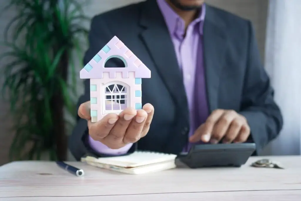 A man off-screen holding a colorful model house