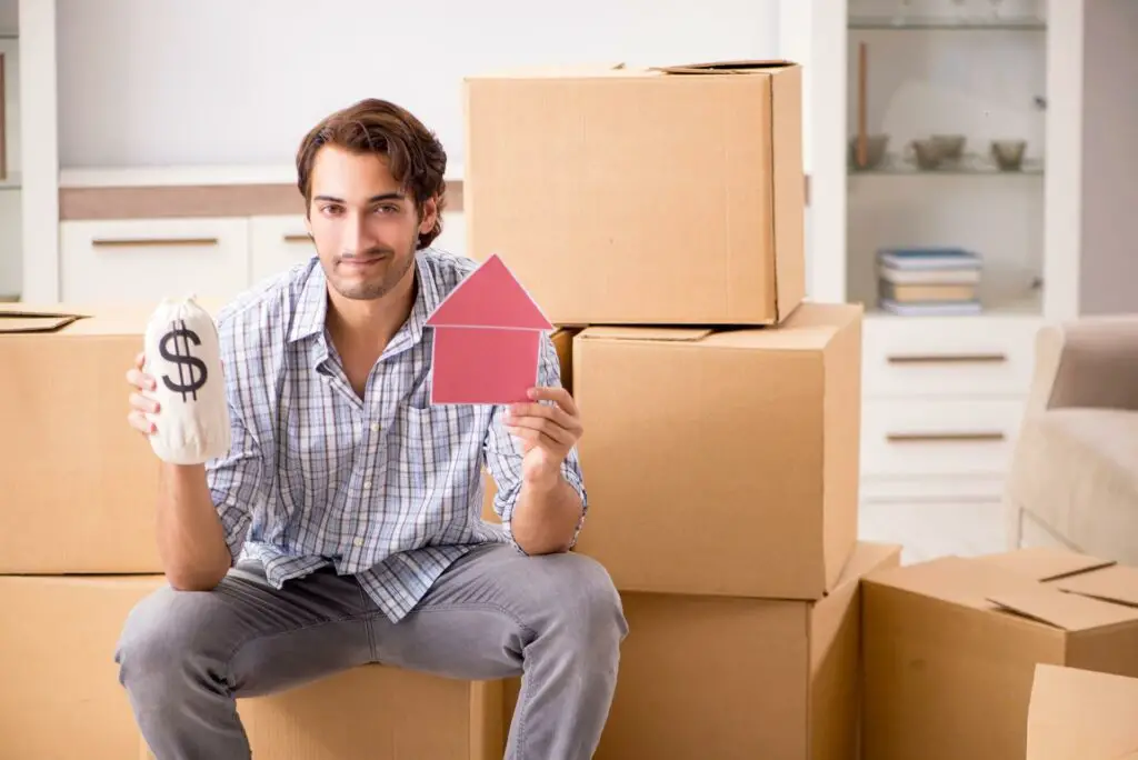 A sitting man holding a cardboard house and money