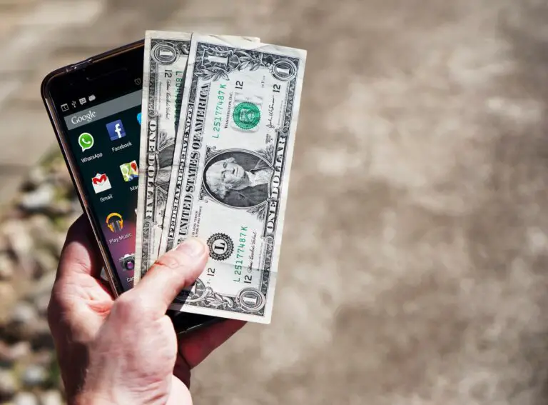 A hand holding cash and a smartphone