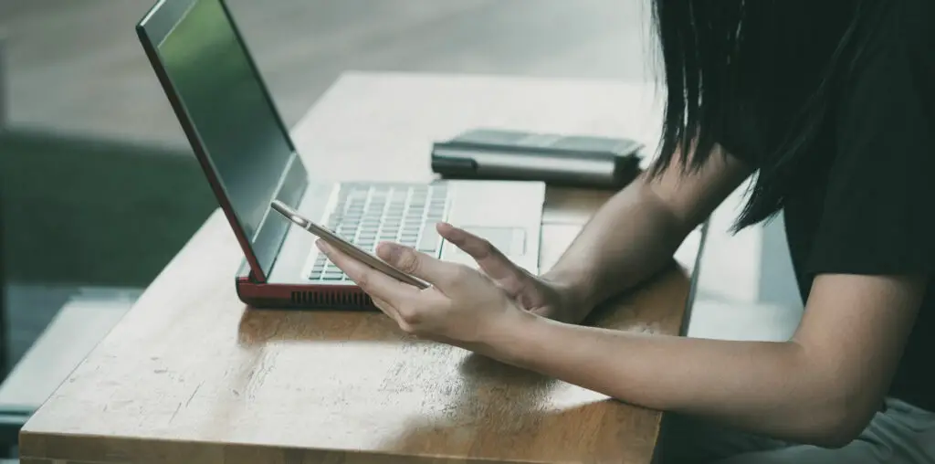 A woman sitting with a laptop and a phone