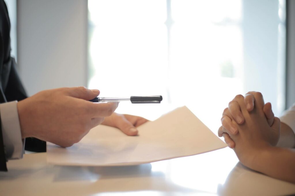 A person passing paper and pen to another person