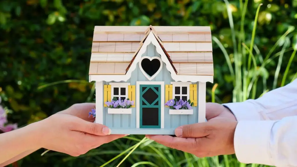 Two individuals holding a model of a house in their hands