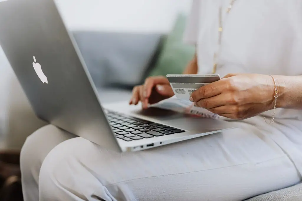 A person typing on a laptop while holding their credit card