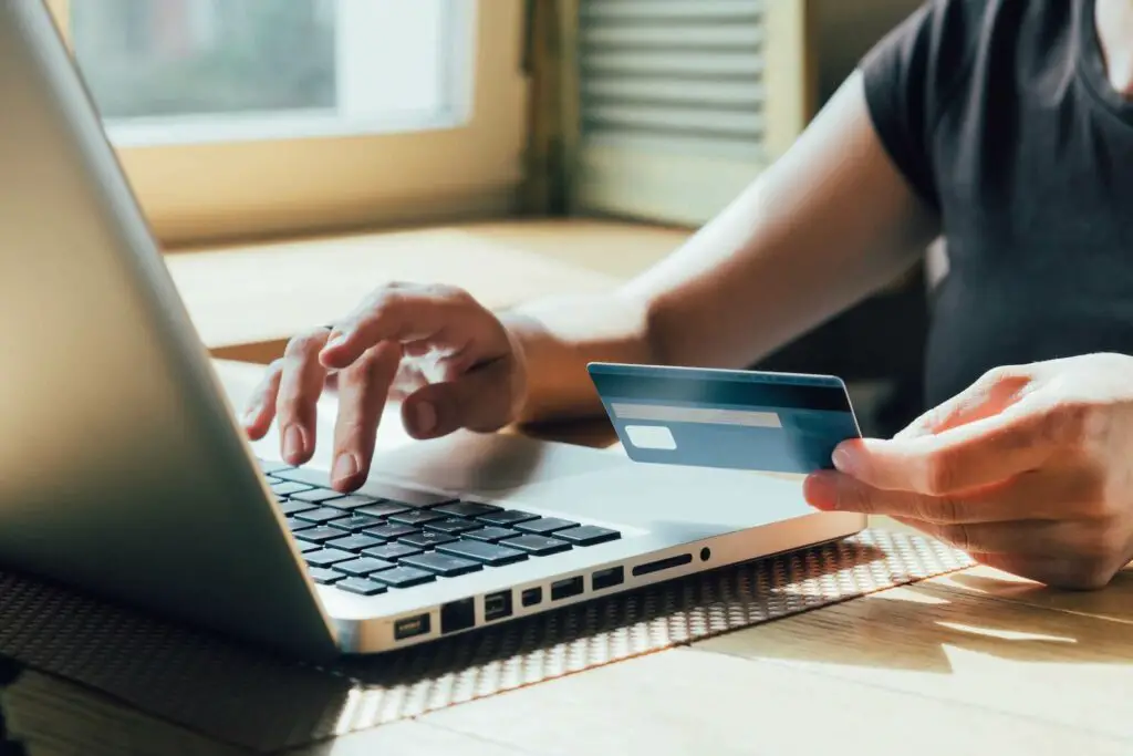 A person holding a credit card and typing on the laptop