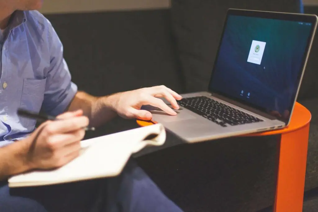  A person writing in a notebook while using a laptop