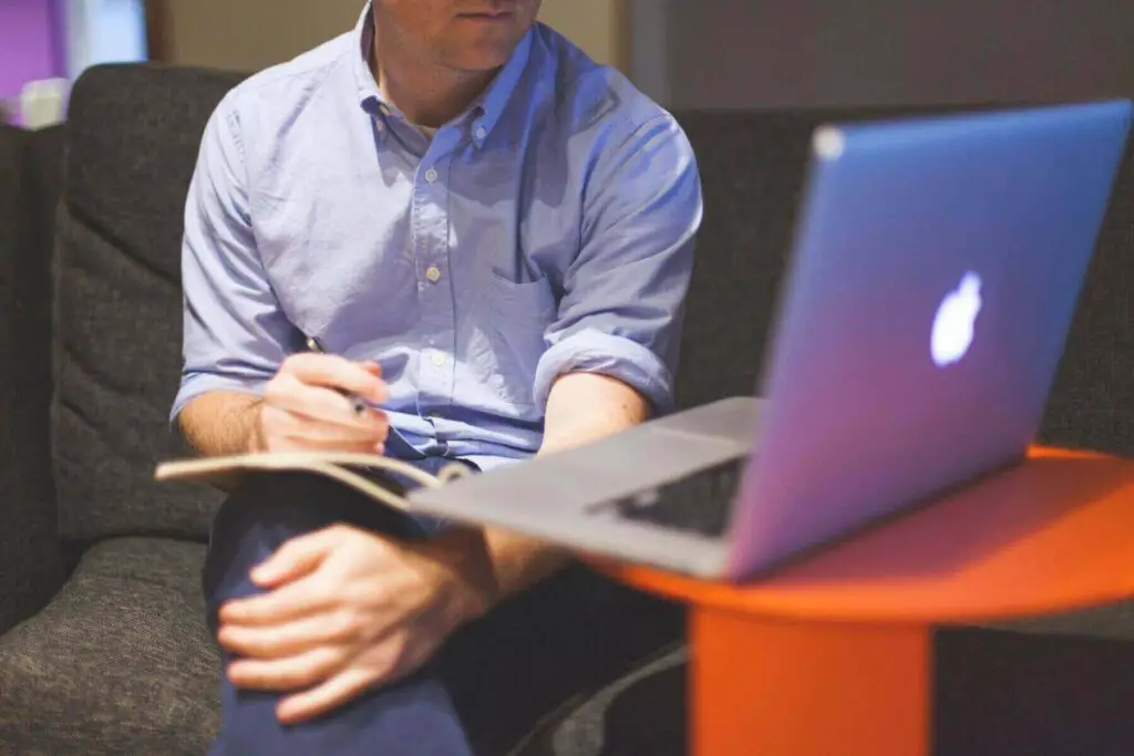 Man taking notes and looking at a laptop